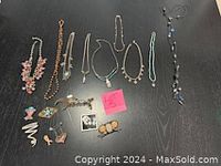 View of nine necklaces displayed with eight assorted pins, showing a mix of bead, silver, and crystal materials, various styles and colors.