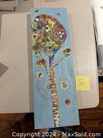 Full view of whimsical oil painting featuring tree with button and collage flowers on a blue background, rectangular shape.