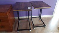 Pair of matching bed tables side by side showing wooden tops and metal frames with caster wheels.