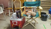 Overview of the camping lot showing the folding chair with green fabric, red cooler, lantern in box, and metal cooking grill.