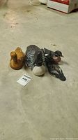 Overview of three wooden bird carvings on floor including a brown duck, loon, and another duck.