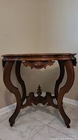Full view front of Victorian style Eastlake walnut table showing curved legs, carved apron, and wood finish.