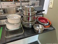 Photo showing stacked stainless steel saucepans with lids and small saucepan, alongside stacked glass and ceramic baking dishes.