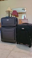 Photo showing both suitcases: gray larger Air Canada suitcase and black smaller Ricardo suitcase on tile floor with lamps and mirror in background