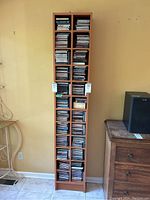 Front view of the tall narrow wooden media shelf filled with CDs, showing its height and compartment layout.