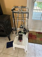 Photo showing folding adjustable walker with wheels and hand grips, black adjustable cane, Revitive Circulation Booster box, and plastic stool with a plastic bin containing bottles of fragrance oils.