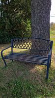 Front view of black hollow metal outdoor bench showing lattice backrest and slatted seat with visible corrosion and bird droppings.