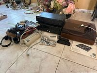Overview of all items on tile floor including turntable, manuals, equalizer, receiver, headsets, cables, power strip, remotes