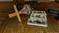 Wooden stereoscope viewer lying on table beside stacks of black-and-white stereo slide cards, showing front view of viewer and cards.