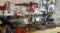 Wide view of the workbench and pegboard showing various hand tools including screwdrivers, pliers, brushes, and hardware in containers.