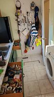Wide view of a narrow utility room with pegboard wall organizing various hand tools, bags, and safety gear. Multiple wooden drawers below pegboard contain additional tools and supplies.