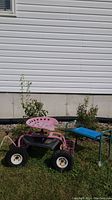 Side view of pink towable tractor seat with rubber tires and wire basket, next to green garden bench with blue seat.