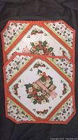 Red background quilted placemat laid flat showing basket with flowers and holly motif in Christmas colors