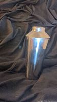 Front side view of stainless steel shaker against dark fabric background showing smooth reflective surface and lid.