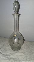 Full view of clear glass decanter with stopper on top, showing bulbous base and long neck.