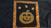 Front view of Halloween quilted wall hanging showing jack-o'-lantern pumpkin, stars, and decorative border.