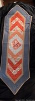 View of the full length of the table runner showing the pointed ends and central diamond and chevron textile pattern in orange and white on blue background.