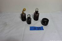Seven-piece set of vintage ruby-colored glass perfume bottles and a small round container displayed on a white cloth background with visible #39 label. Includes multiple sizes, some with faceted stoppers and a damaged atomizer pump.