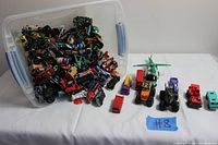 Plastic container tipped over spilling numerous small toy cars, toy soldiers, and a toy helicopter on table.