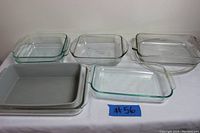 Six baking pans and ovenware pieces, mostly glass but some metal, arranged on a flat surface shown from above, demonstrating the lot contents.
