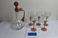 Photo showing one clear crystal glass decanter with matte brown stopper and handle and five matching wine glasses with brown twisted stems and clear bowls with spiral pattern.