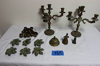 Overview of vintage brass lot including two 4-arm candelabras, three brass bells, six brass leaf-shaped ornaments, and several brass candle cups.