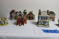 Several Christmas village houses including a palace dance hall, saloon, village news building, and other cottages arranged on a white surface with lot number #47.