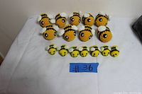 16 handmade crochet bees displayed on a white surface: 8 larger bees at back and 8 smaller bees in front, all yellow with black stripes, white wings, and black eyes.