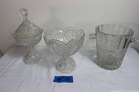 Front view of two crystal compotes and one clear frosted glass ice bucket on white cloth