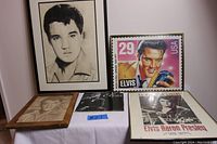 Lot of five framed Elvis Presley memorabilia items arranged on a table including a charcoal portrait, stamp-like print, vintage photo, calendar and poster.