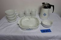 Front view showing all items in the lot arranged including CorningWare coffee pot, casserole dish with lid, Glasbake bowls and cups with lids.