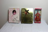 Photo of three boxed Barbie dolls standing side by side on white fabric background, showing original packaging and doll details.