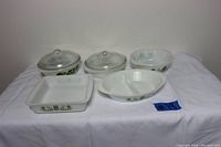Five Glasbake green floral daisy casserole dishes, two with glass lids, arranged on white cloth background.