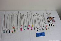 Entire lot of hand blown glass necklaces with figurine pendants and loose glass figurines displayed on white surface.