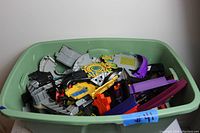 Green plastic tub filled with assorted Hot Wheels track parts and accessories showing various colors and shapes.