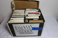 Box full of miscellaneous books all stacked upright with visible edges and assorted colors in cardboard box.