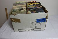 Cardboard storage box containing a mix of books and VHS tapes.