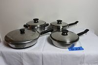 Top view of 8 vintage cookware pieces including pots, fry pans, lids, and a large skillet