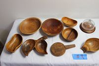 Front view of all 11 wood dishes and bowls laid out on white cloth showing various shapes and sizes.