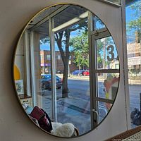 Full view of the round mirror mounted on a wall reflecting outdoor and indoor elements.