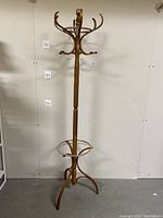 Full view of the vintage wooden coat rack showing its height, curved hooks, and tripod base with umbrella holder.