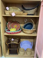 A wooden cabinet shelf displaying a large assortment of baskets made from wicker, rattan, and handwoven dyed materials. Varied colors include natural browns, vibrant yellows, blues, and multicolor patterns.