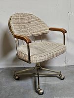 Front side view of the mid-century modern swivel chair showing oatmeal fabric seat and back with brass frame and caster wheels.