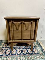 Front view of the mid-century modern wooden side table showing the decorative front panel with carved arches and the tapered legs, placed on a patterned rug.