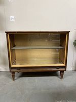 Front view of the wooden Mid Century Modern bar cabinet with glass door and mirror inside, showing the glass shelf and interior.
