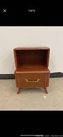 Front view of Mid Century Modern style wooden side table with one open shelf and one drawer with brass handle, standing on four tapered legs.