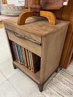 Side view of walnut side table showing open shelf filled with books and drawer above.