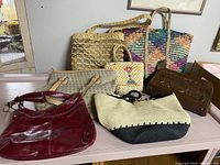 Seven assorted purses of different materials and colors arranged on a table