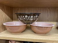 Three nesting bowls on a wooden shelf, two pink and one brown with white floral pattern on exterior.