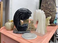 Angled view of assorted stone sculptures including black animal head, white arch, and partial view of others on a shelf